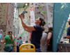 Kletterin hält Handy in Boulderhalle in Wien, im Hintergrund klettern andere Personen.