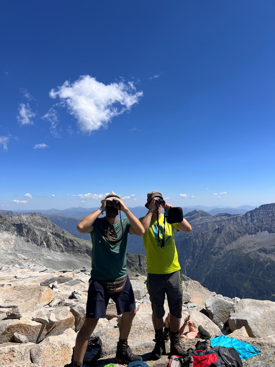 Zwei Männer mit Ferngläsern auf felsigem Berggipfel in den Alpen